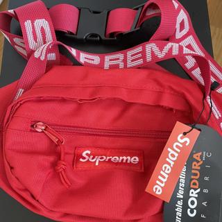 Man in pink shirt with red Supreme bag in hand walks towards