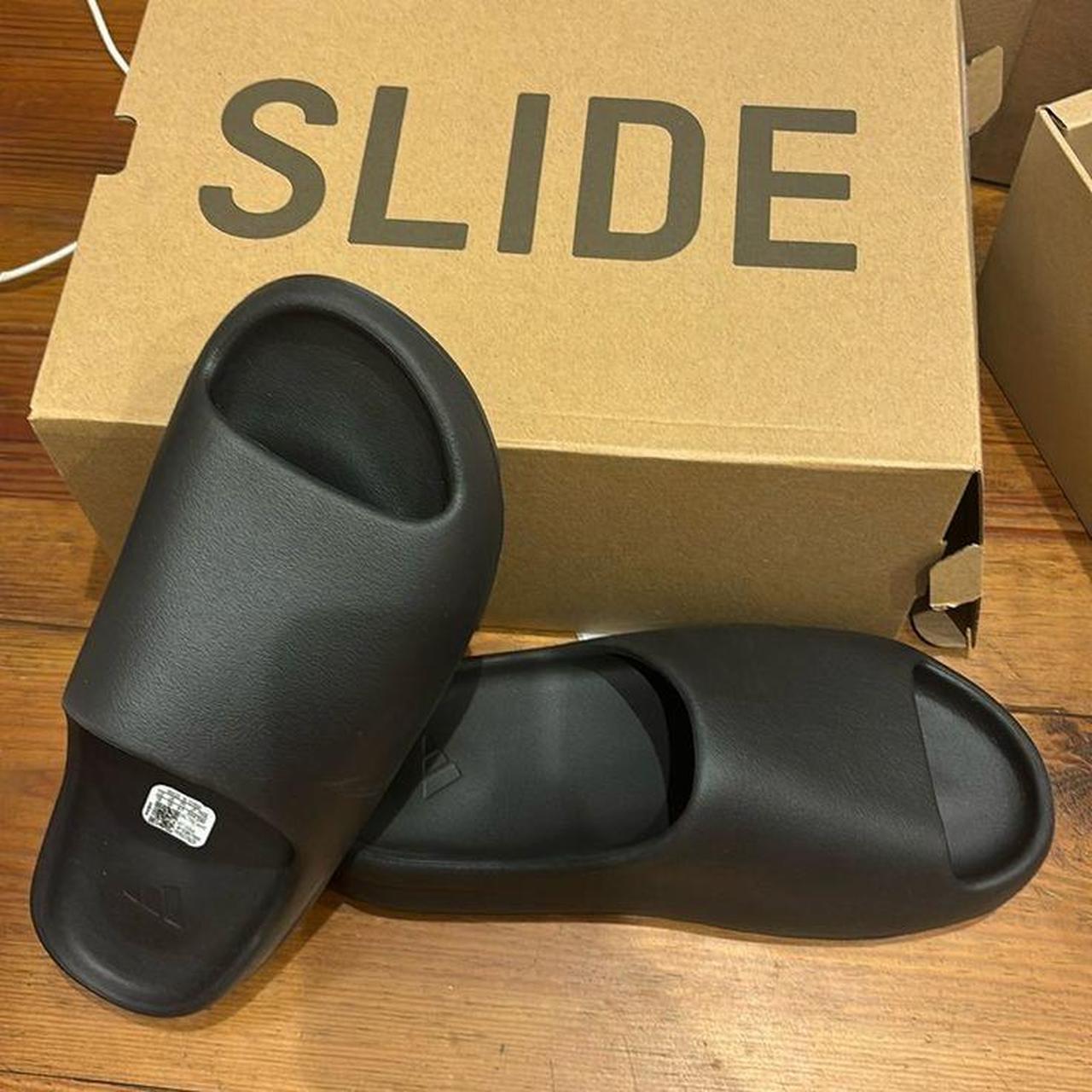 The black Yeezy Slide features a minimalist design... Depop