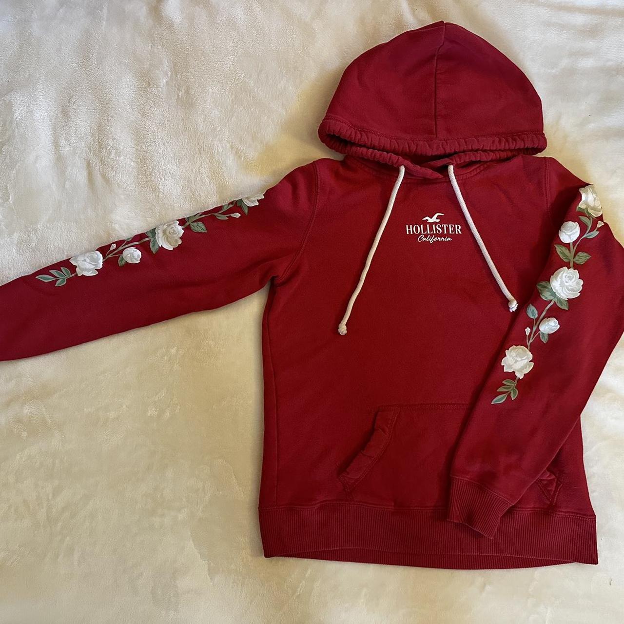 Red Hollister hoodie with white rose design on the. Depop